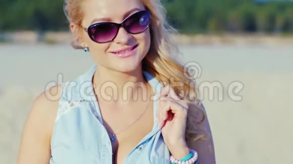 性感的金发女郎戴着太阳镜在海滩上摆着相机视频的预览图