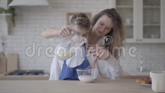 肖像可爱的儿子在厨房帮妈妈这个男孩用胡须干扰玻璃碗里的牛奶视频的预览图