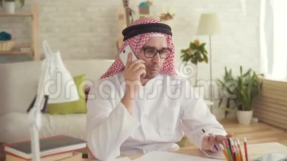 坐在桌子旁用智能手机说话的阿拉伯男人视频的预览图