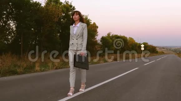 美丽的女人在路上徒步旅行一个女商人穿着轻便的西装走在沥青上提着一个黑色的公文包视频的预览图