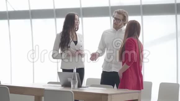 一位戴眼镜的商人一边打手势一边向站在大公司前面的两位女同事解释他的想法视频的预览图