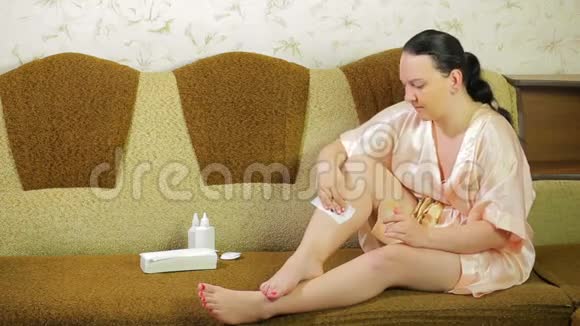 年轻的黑发女人在家里用蜡和餐巾脱毛腿视频的预览图