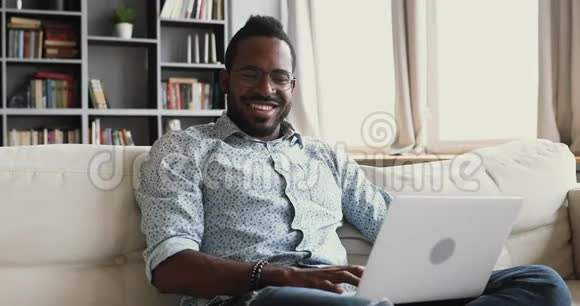 快乐的非洲人使用笔记本电脑上网坐在沙发上视频的预览图