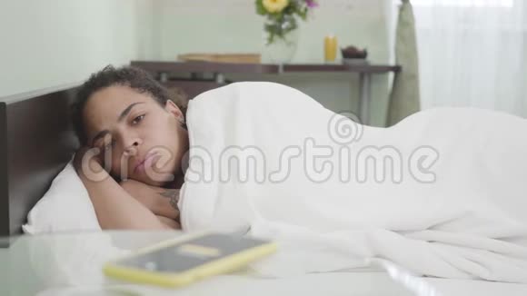 漂亮的非洲裔美国妇女睡在白色毯子下在灯光室的背景警报响了视频的预览图