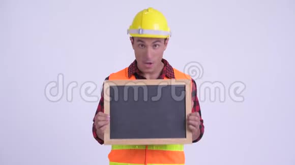 年轻快乐的西班牙裔建筑工人拿着黑板看上去很惊讶视频的预览图