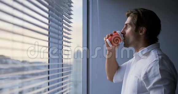 年轻的高加索男性高管在现代办公室窗户附近喝咖啡的侧视图视频的预览图