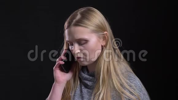黑色背景下金发女孩在智能手机上认真说话的肖像视频的预览图
