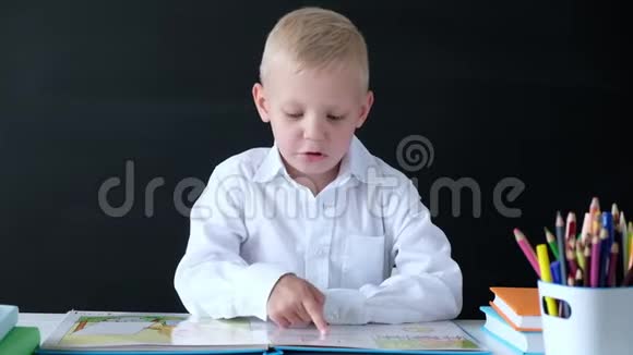 可爱的小男孩坐在桌子旁看书小学的孩子教育观念回学校去视频的预览图