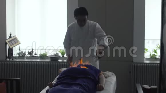 在中国的一次火灾按摩中一个亚洲男人在毛巾上点燃液体把液体倒在躺着的人身上视频的预览图