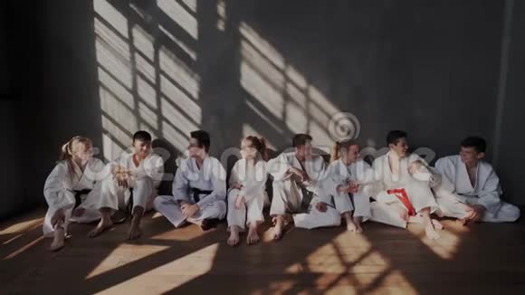 跆拳道学校的青少年在经过紧张的武术训练后放松他们白坐在墙边聊天视频的预览图