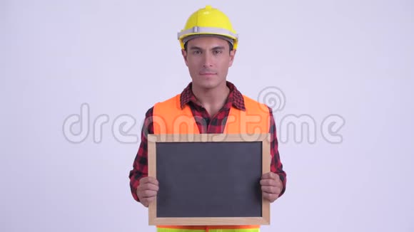 年轻快乐的西班牙裔建筑工人一边拿着黑板一边思考视频的预览图