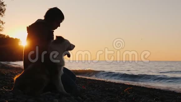 一个人坐在他的狗旁边一起看着湖面或大海上的日落视频的预览图