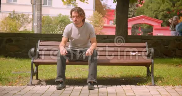 可爱的白种人坐在户外公园的长凳上的特写照片视频的预览图