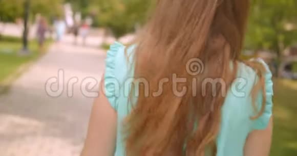 在公园里一位年轻的长发美丽的女性在风中谄媚地散步视频的预览图