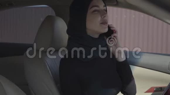 独立的年轻穆斯林妇女坐在她的车里看着自己在米尔里尔和谈话的画像视频的预览图