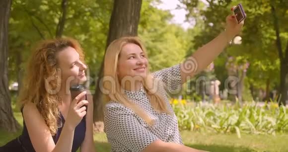 两位女朋友在公园户外坐在毯子上打电话自拍的特写照片视频的预览图
