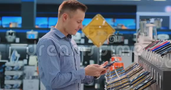 年轻的帅哥穿着蓝色衬衫在一家电子商店里选择了一部新手机现代技术采购视频的预览图