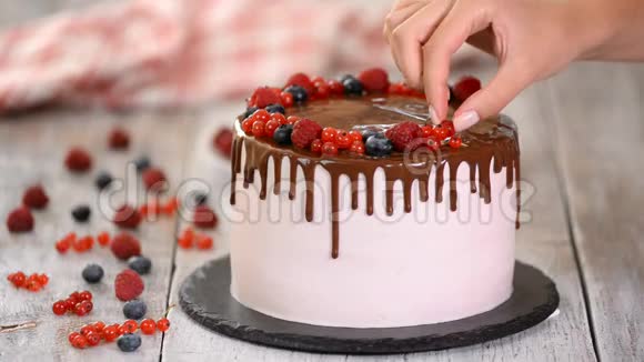 糖果师用浆果装饰饼干蛋糕蛋糕上有粉红色的奶油和巧克力蛋糕放在木架上视频的预览图