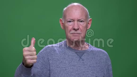 一个老白种人的特写镜头他伸出大拇指看着一台与绿色隔离的背景相机视频的预览图