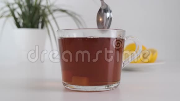 用金属勺子将搅拌好的糖用透明的玻璃杯茶放在白色的桌子上慢动作视频的预览图