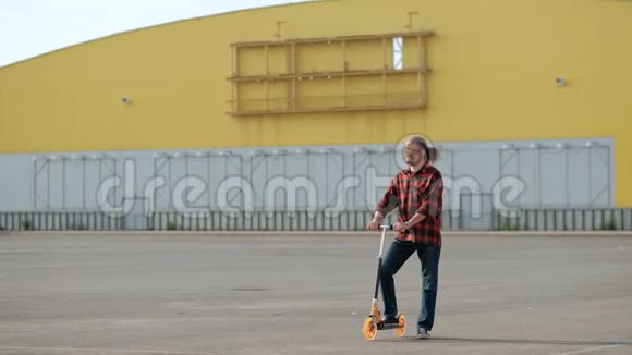 穿着一件格子红色衬衫的长灰发的中年男子骑着一辆踢踏板车轻松迷人视频的预览图