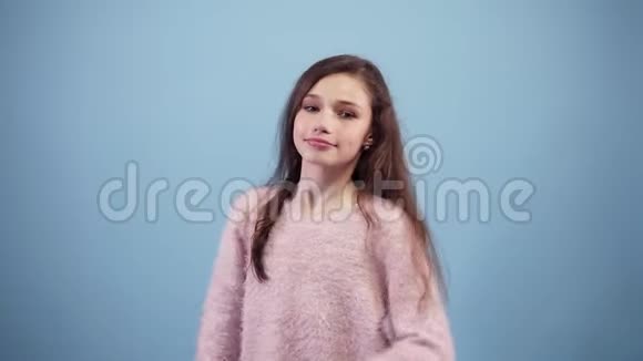 年轻漂亮的长发女孩在一个蓝色的背景上微笑和开玩笑跳舞穿着鲜艳的粉色视频的预览图