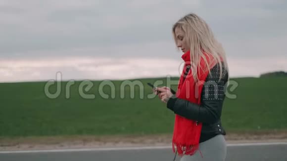 金发女人在路上行走使用智能手机戴着红领巾的女孩看着电话视频的预览图