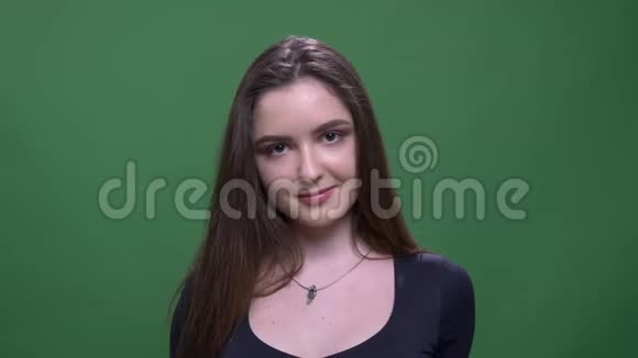 年轻漂亮的深色头发的年轻女性的特写肖像带着羞怯的微笑她的头发正盯着背景的相机视频的预览图