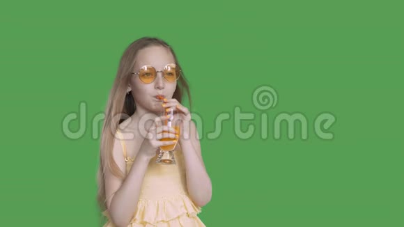 少女在透明的绿色背景下用玻璃吸管喝橙汁年轻女孩享受新鲜享受视频的预览图