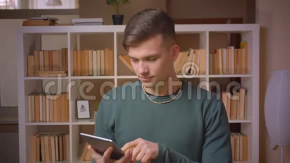 在平板电脑上打开应用程序的年轻男学生的肖像显示了它的绿色彩屏并在图书馆竖起大拇指视频的预览图