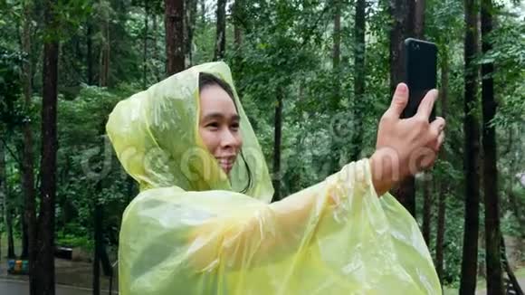 下雨天亚洲年轻女子在松林用智能手机自拍视频的预览图