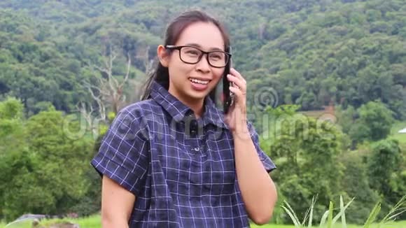 亚洲年轻的女人在电话里讲话举起手臂看着大自然背景上的成功视频的预览图