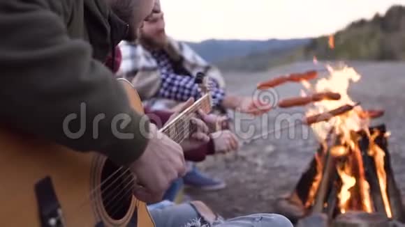 晚上在山上用篝火和烹饪香肠野餐年轻人快乐的朋友唱歌视频的预览图