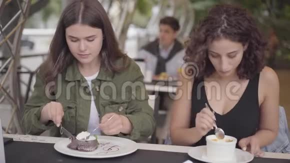 两个女朋友坐在户外咖啡馆吃蛋糕的肖像年轻女孩一起享用美食一起分享视频的预览图