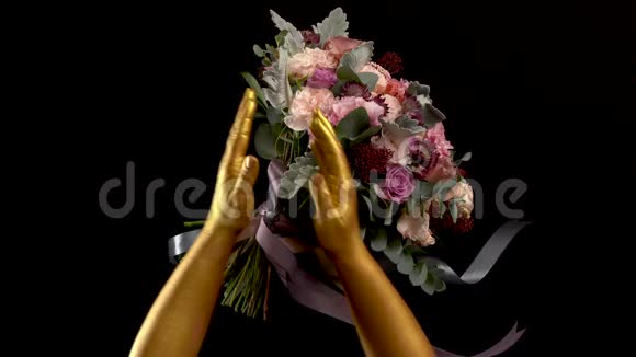 女人的金手拿着花束把它举到相机上把花束合上手画成金色视频的预览图