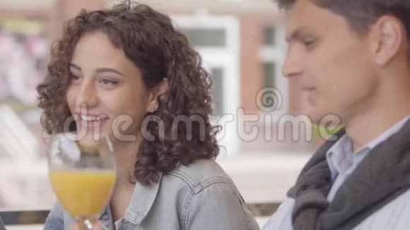 一对夫妇在户外咖啡馆喝橙汁时谈笑风生的肖像年轻男女视频的预览图