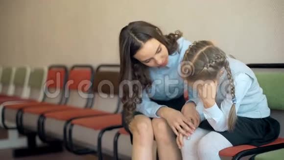 一位女老师坐在走廊里安慰一个年轻的学校伤心的女孩视频的预览图