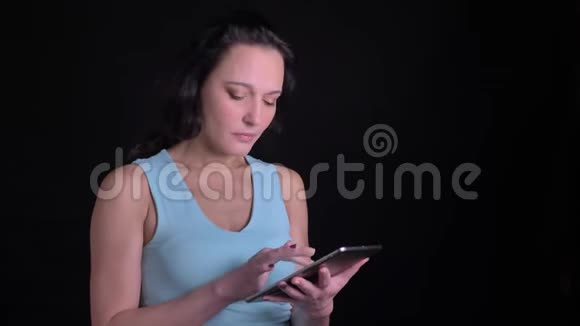 中年妇女在黑色背景下以极大的兴趣和惊喜观看平板电脑的肖像视频的预览图