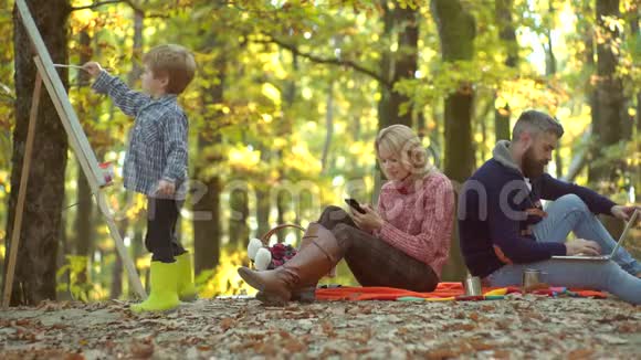 幸福的家庭一起在黄色的自然快乐微笑的年轻父母和小儿子躺在秋叶里快乐的孩子视频的预览图