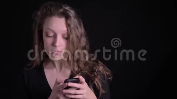 年轻卷发女孩专注地看着智能手机的肖像在黑色背景上显示出惊喜视频的预览图