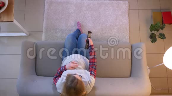 年轻孕妇坐在沙发上拿着电视看电视的特写镜头视频的预览图