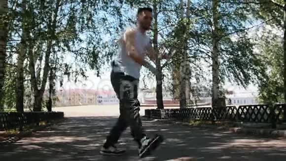 年轻迷人的男子纹身自由式舞蹈在公园和步行向前建筑物的背景视频的预览图