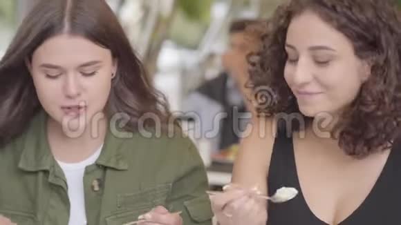 两个女朋友坐在户外咖啡馆吃蛋糕的肖像年轻女孩一起享受他们的晚餐聊天和聊天视频的预览图