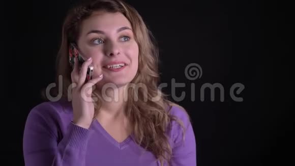 在黑色背景下一个快乐的金发女人在智能手机上打电话的肖像视频的预览图
