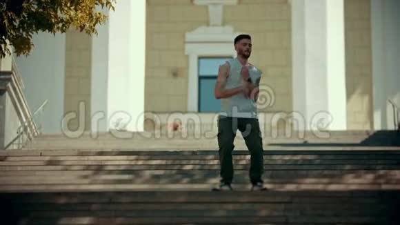 年轻时尚的男子穿着白色衬衫在楼梯上跳舞背景是一栋建筑视频的预览图