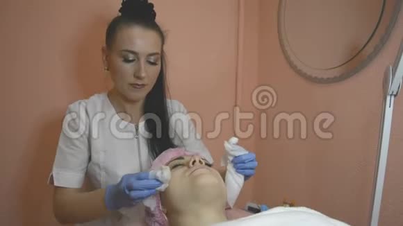 年轻女子躺在专业美容师和皮肤科医生诊所的沙发上女医生清洁皮肤视频的预览图