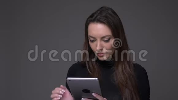 美丽的黑发女人将绿色的平板电脑屏幕显示成相机以推荐隔离在灰色上的应用程序视频的预览图