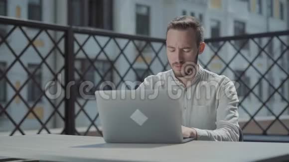 有胡子的自信的年轻人坐在笔记本电脑前的露台上的桌子旁工作自由职业概念视频的预览图
