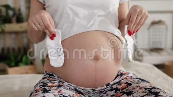 孕妇裸腹为未来新生男婴或女孩准备的袜子视频的预览图