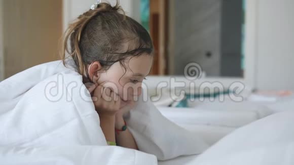 小女孩躺在床上躺在毯子下在电子平板上看动画片视频的预览图